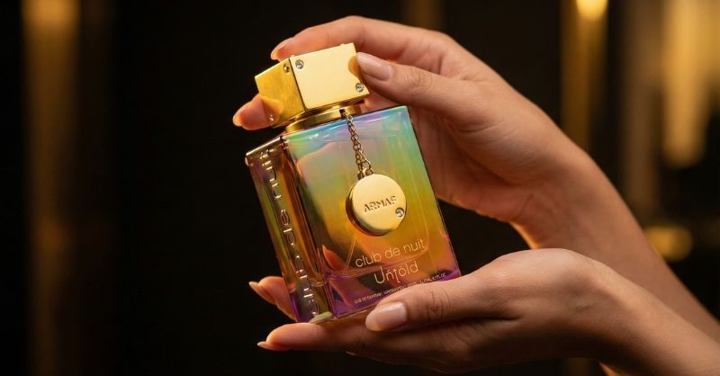 Frasco holográfico do perfume Armaf Club de Nuit Untold sendo segurado em ambiente luxuoso.